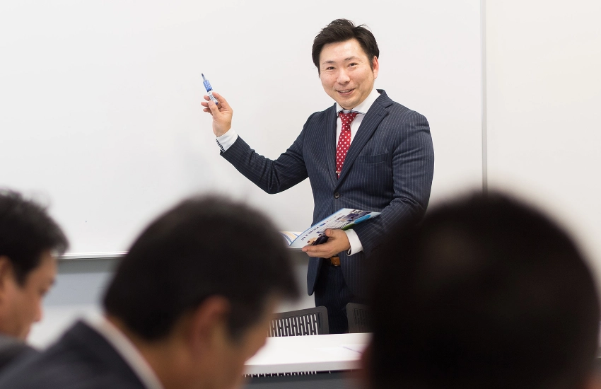 会議室でホワイトボードを使い、メンバーやクライアントに向けて笑顔でプレゼンテーションを行うS.T.さん